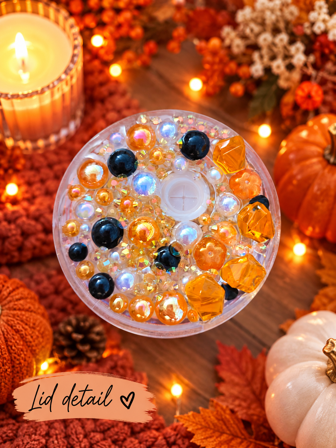 A circular clear tumbler lid filled with decorative glass beads, amber faceted ornaments, and dark blue beads, styled in an autumn setting with a lit candle, pumpkins, fall leaves, and warm string lights. A label at the bottom reads 'Lid detail'.