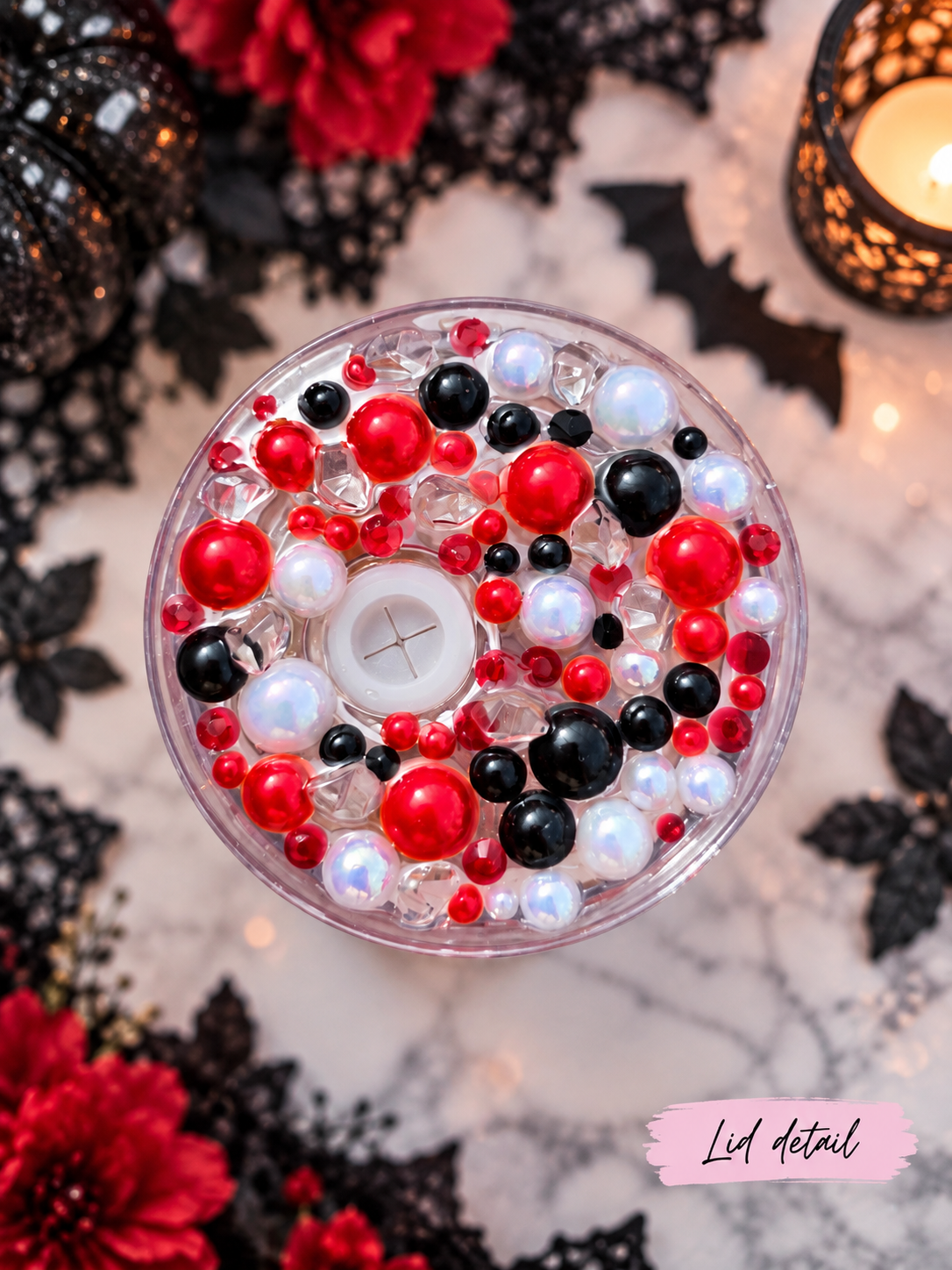 Top-down view of a clear round tumbler lid with red, black, and white decorative beads and pearls, with a white button in the center. The scene is styled with red flowers, black lace, bat cutouts, and a lit candle, with a pink label reading 'Lid Detail' in the bottom right corner.
