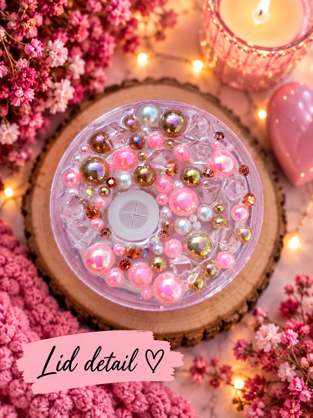 A top-down close-up of a round lid filled with pink and iridescent beads and pearls, labeled 'Lid detail' on a pink banner. The scene is styled with pink flowers, a lit candle, warm fairy lights, and a pink heart on a light surface.