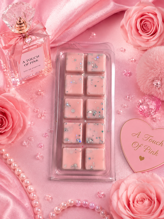 Pink wax melts in a clear plastic tray, styled on pink satin with pink roses, pearls, a perfume bottle labeled 'A Touch of Pink,' and a heart-shaped card reading 'A Touch of Pink.'.