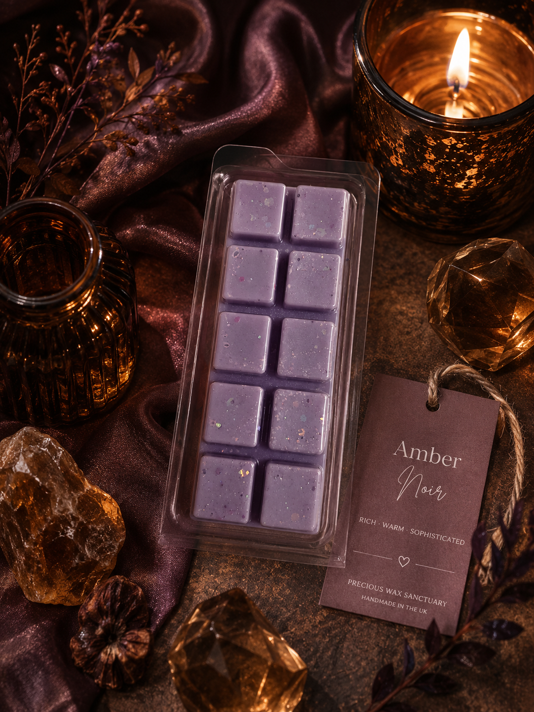 A packaged wax melt bar labeled 'Amber Noir' by Precious Wax Sanctuary, shown in a clear plastic clamshell with a matching paper tag. The wax is a muted lavender-purple color with tiny glitter flecks.