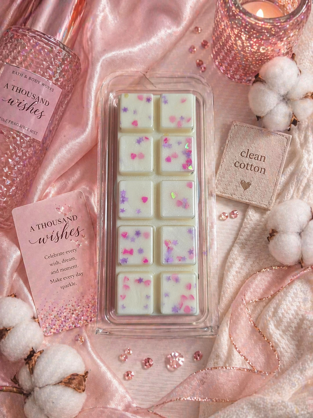 Packaged wax melts with 'A Thousand Wishes' and 'Clean Cotton' labels on a pink fabric background.