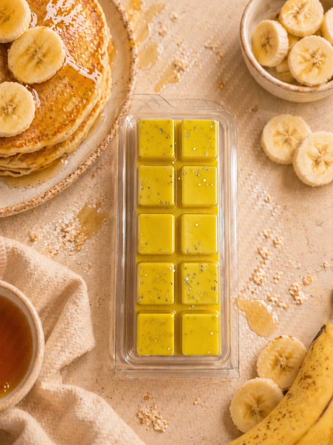 Wax melts with a stack of pancakes, sliced bananas, and a bowl of honey on a beige surface.