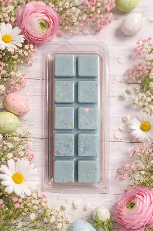 Pack of blue square wax melts surrounded by flowers on a light wooden surface
