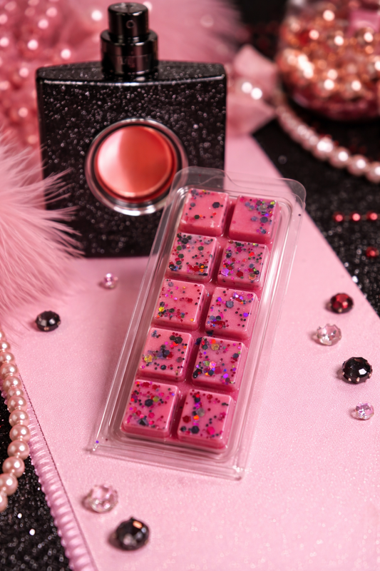Pink wax melts in a clear container with a black glittery lip gloss on a pink surface.