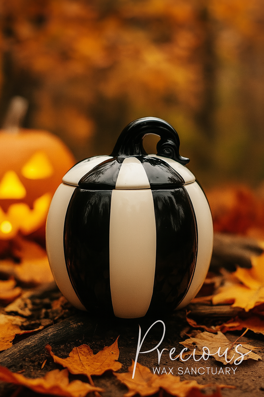 Black and white striped pumpkin-shaped candle on a wooden surface with blurred autumn background