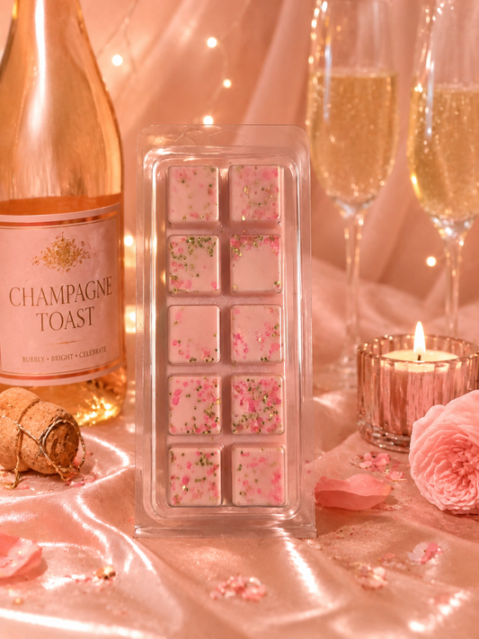 Pink champagne toast wax melt with a bottle of champagne and glasses in the background.