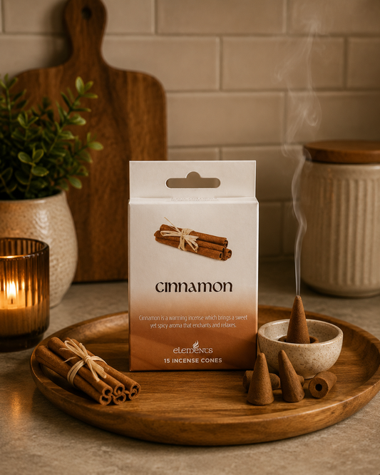 A package of Elekes Cinnamon incense cones stands on a wooden tray, surrounded by loose cinnamon sticks, a burning incense cone in a small bowl with visible smoke, and warm ambient lighting in a kitchen-like setting.