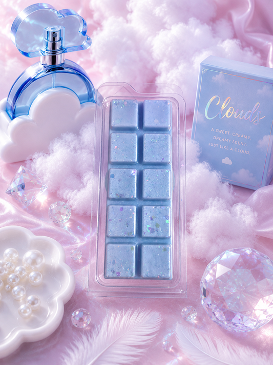 A light blue cloud-shaped perfume bottle and a matching cloud box labeled 'Clouds' are arranged with fluffy pink fabric, white feathers, pearl dish, and clear decorative crystals around a central clear-wrapped rectangular product with blue wax melt bar.