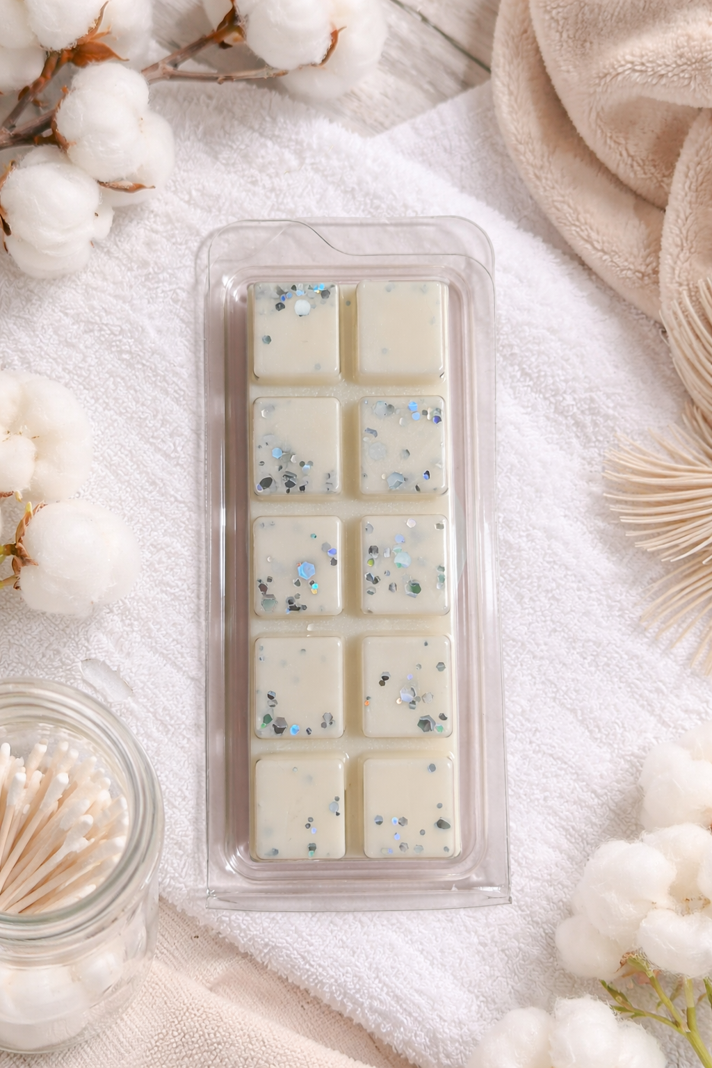 white wax melt bars embedded with small specks, surrounded by cotton flowers and a wooden stick container.