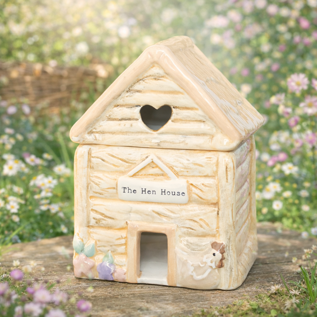 Decorative ceramic wax and oil hen house with a heart-shaped window on a wooden surface with a garden background.