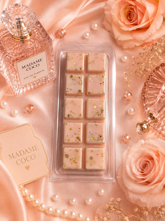 Madame Coco wax melts in a clear plastic tray, styled on a pink satin background with a perfume bottle, pearls, roses, and decorative accessories.