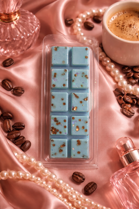 Blue wax melts in a mold on pink satin with coffee beans, pearls, and a cup of coffee.