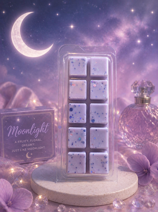 A packaged wax melt or scented melt bar set displayed on a round pedestal against a dreamy purple galaxy night-sky background with a crescent moon, stars, flowers, and a perfume bottle. The main product is a clear plastic clamshell containing nine pale lavender square wax melts with blue and purple glitter flecks.