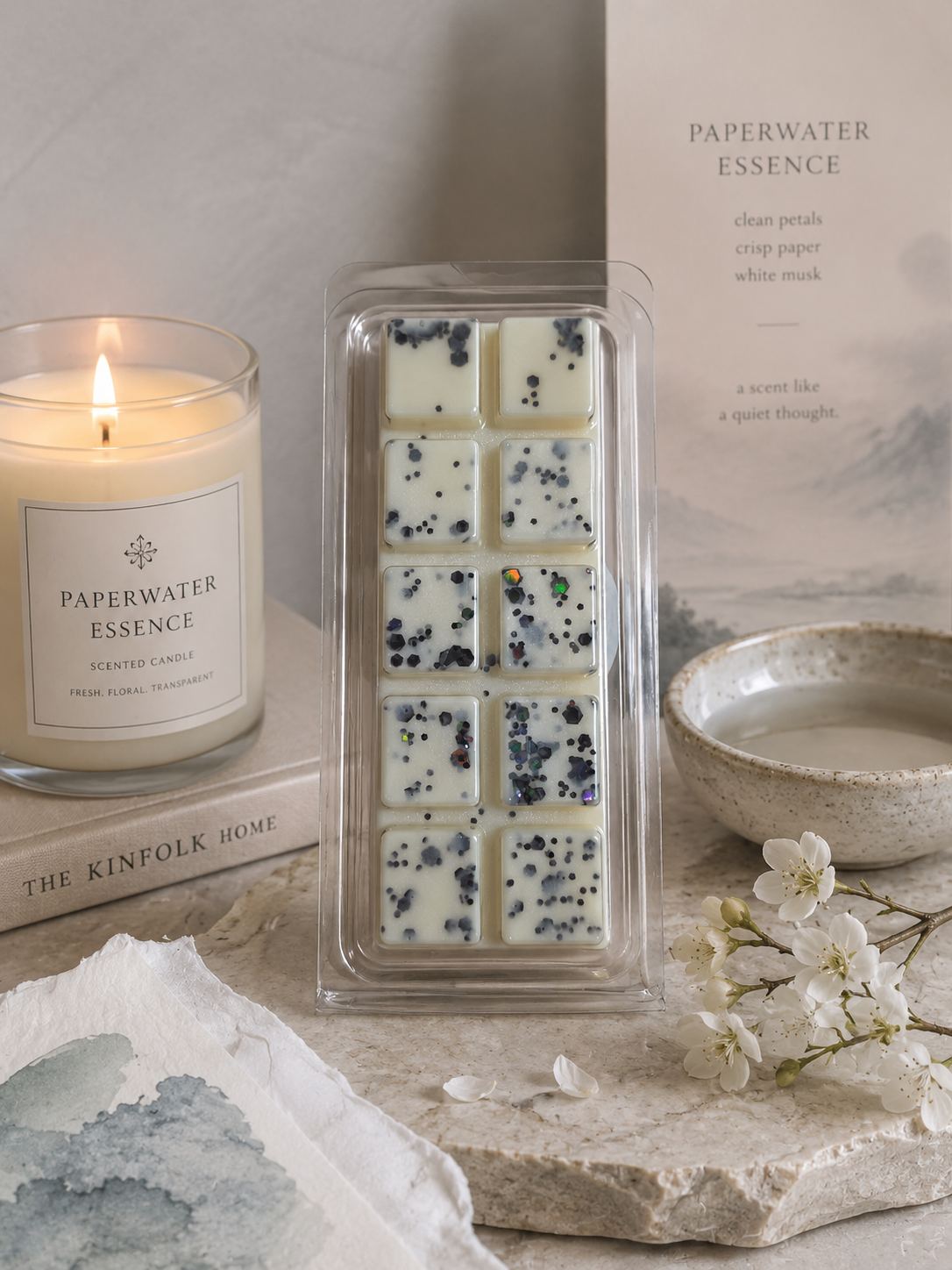 Candle with 'Paperwater Essence' packaging, wax melt, and a bowl on a neutral background.