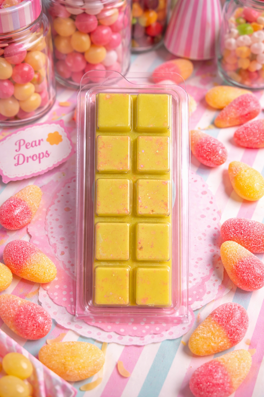Yellow wax melt bar in a pink packaging surrounded by colorful candies on a patterned surface.