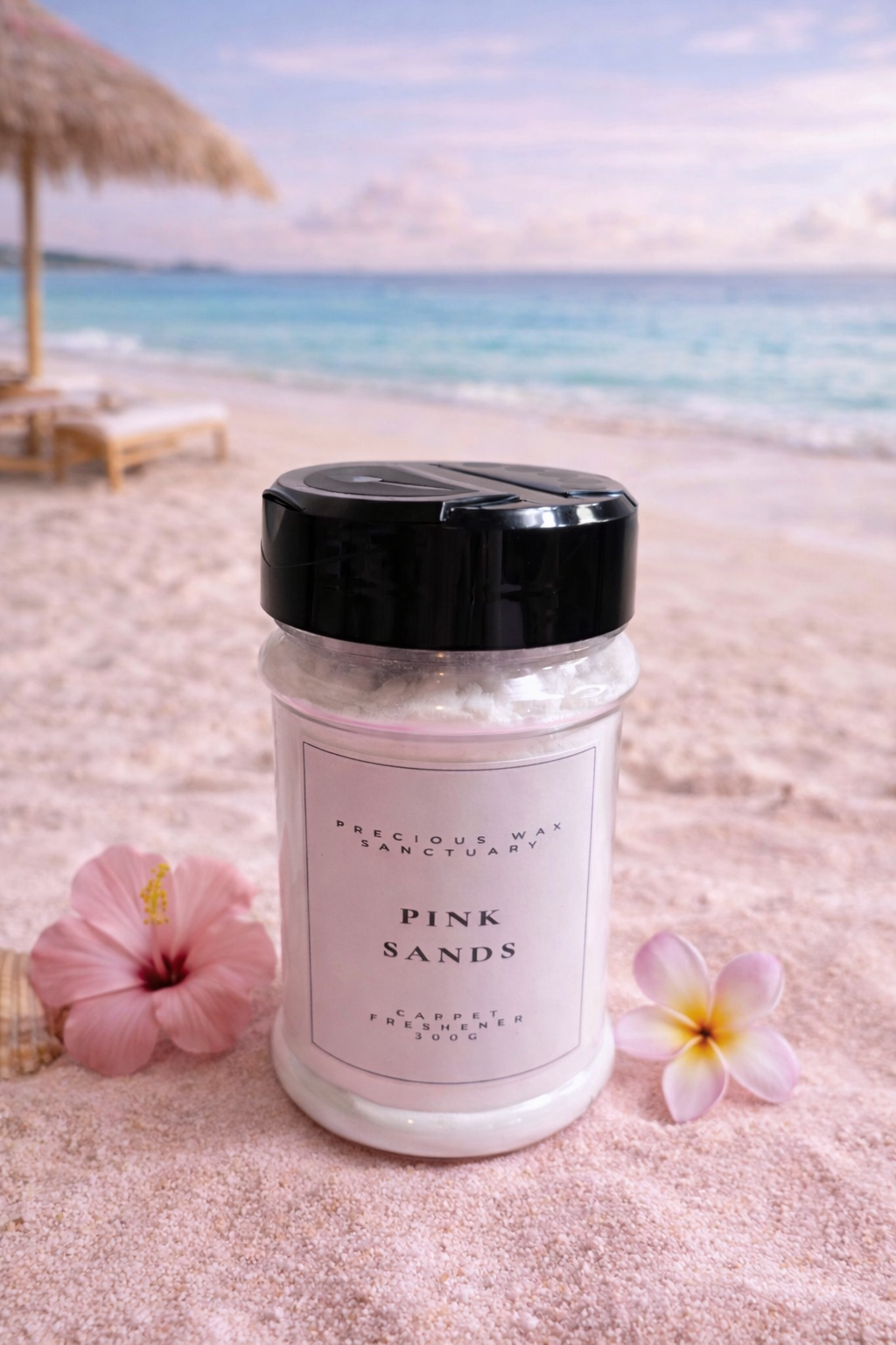 Jar of 'Pink Sands' carpet freshener on a sandy beach with flowers and ocean view