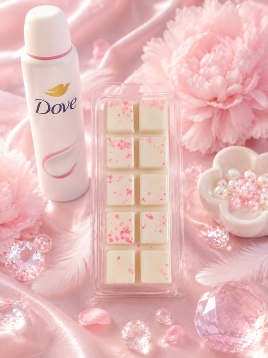 Dove body wash bottle next to a clear plastic container of wax melts with pink floral speckles, styled on pink satin with flowers, feathers, and crystals.
