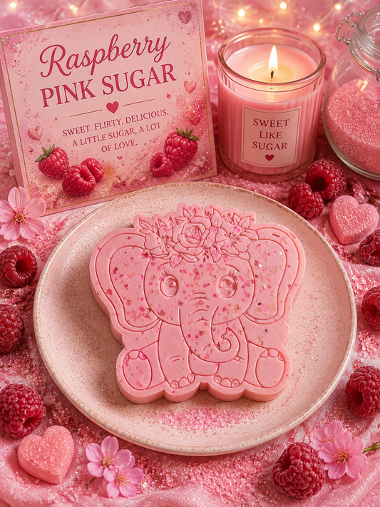 A pink elephant-shaped wax melt sits on a light beige plate, surrounded by pink sugar, raspberries, flowers, and a pink candle. A branded box reading 'Raspberry Pink Sugar' is visible in the background.