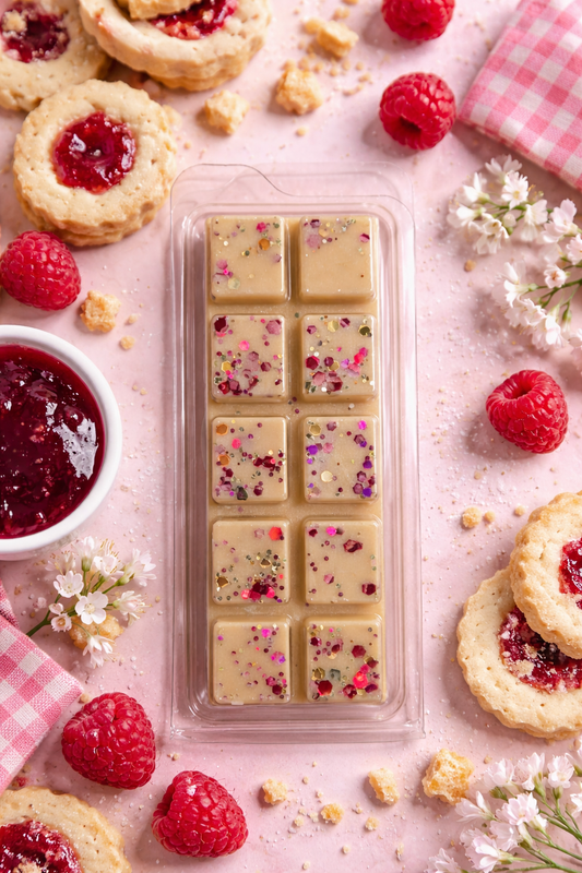 Wax melts surrounded by raspberries and cookies on a pink surface.
