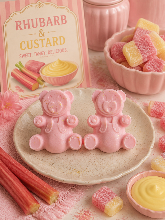 Two pink teddy bear-shaped wax melts displayed on a beige plate, with a pink and white 'Rhubarb & Custard' box in the background, rhubarb sticks, pink and yellow sugar cubes, and a pink bowl of custard in a styled setting.