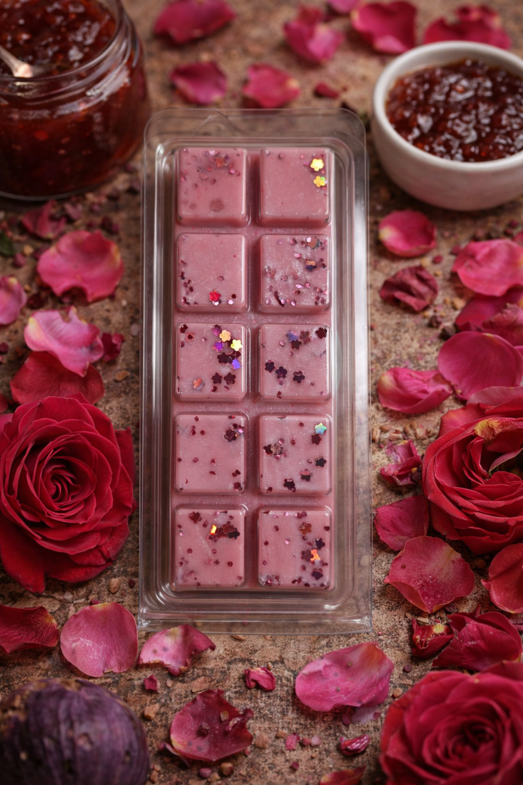 Pink wax melts in a mold surrounded by red roses and rose petals on a textured surface.