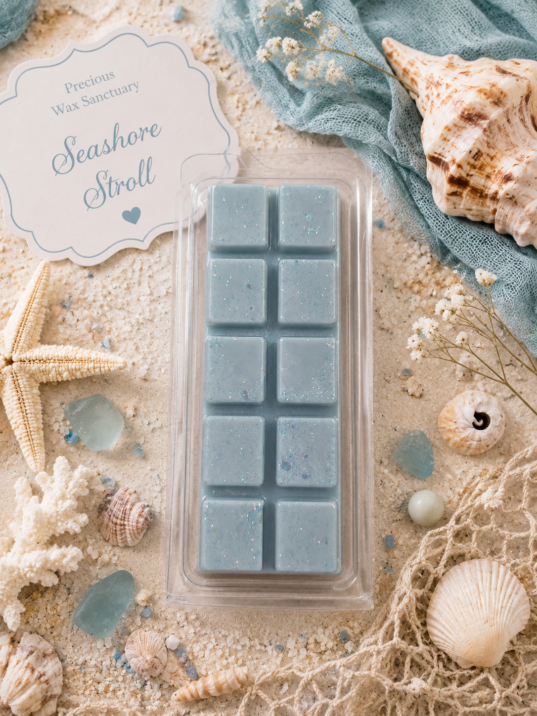 A wax melt bar set in a clear plastic clamshell package, placed on a sandy beach-themed background with seashells, a starfish, blue fabric, and a printed label reading 'Precious Wax Sanctuary Seashore Stroll'.