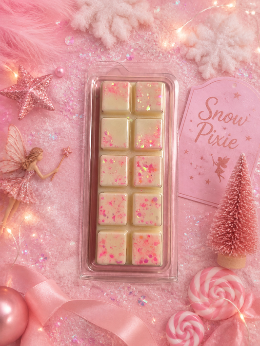 A clear plastic clamshell package wax melts, each speckled with pink glitter, displayed on a pink glittery background with decorative holiday and fairy props.