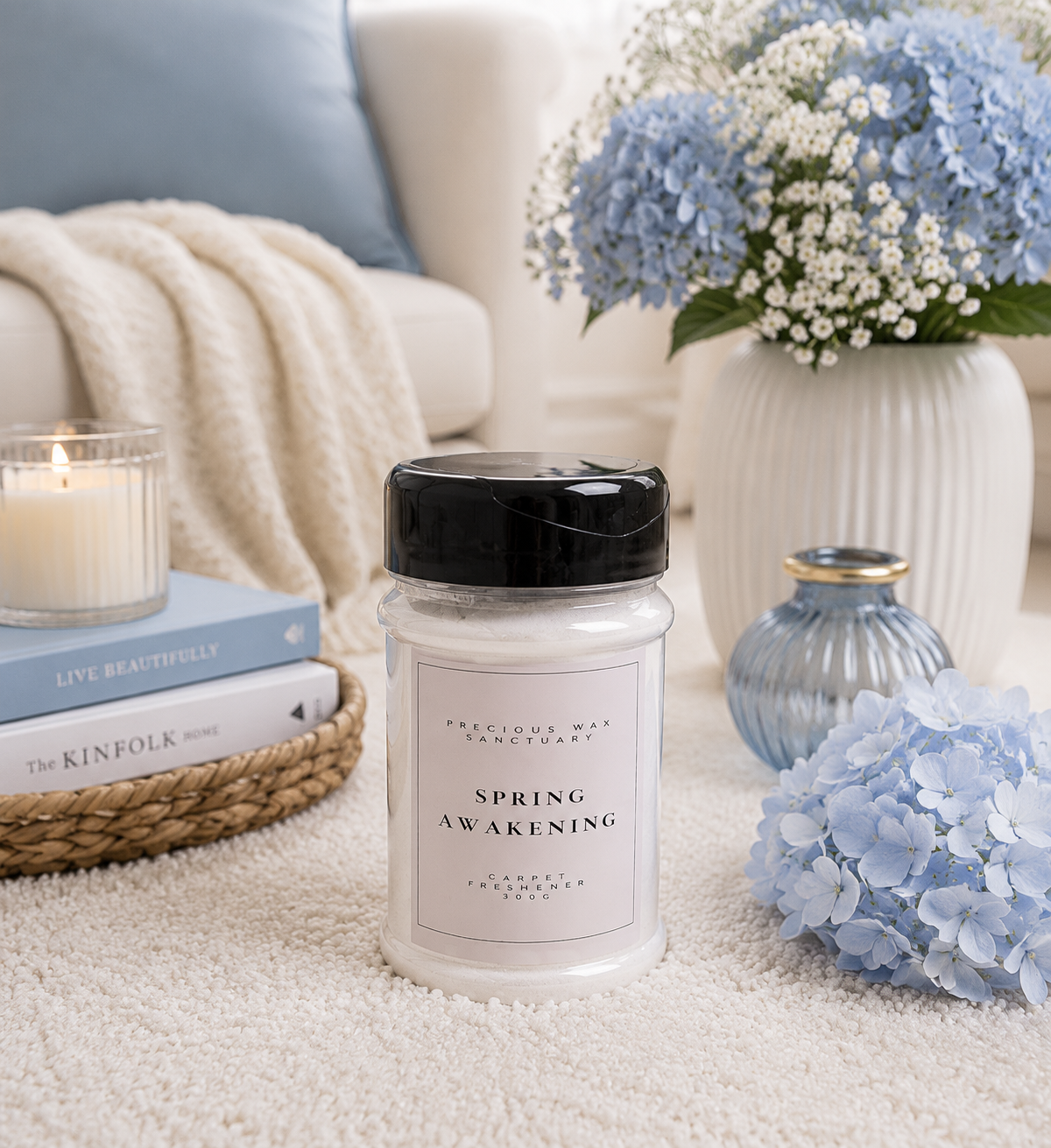A jar of carpet freshener labeled 'SPRING AWAKENING' by Precious Wax sanctuary sits on a cream rug in a styled living room setting with a candle, books, flowers, and a throw blanket.