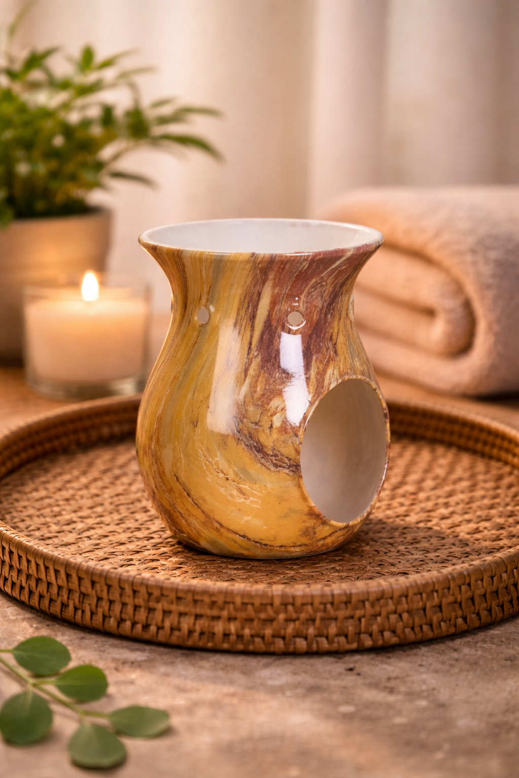 Decorative wax burner on a woven tray with a candle and plant in the background