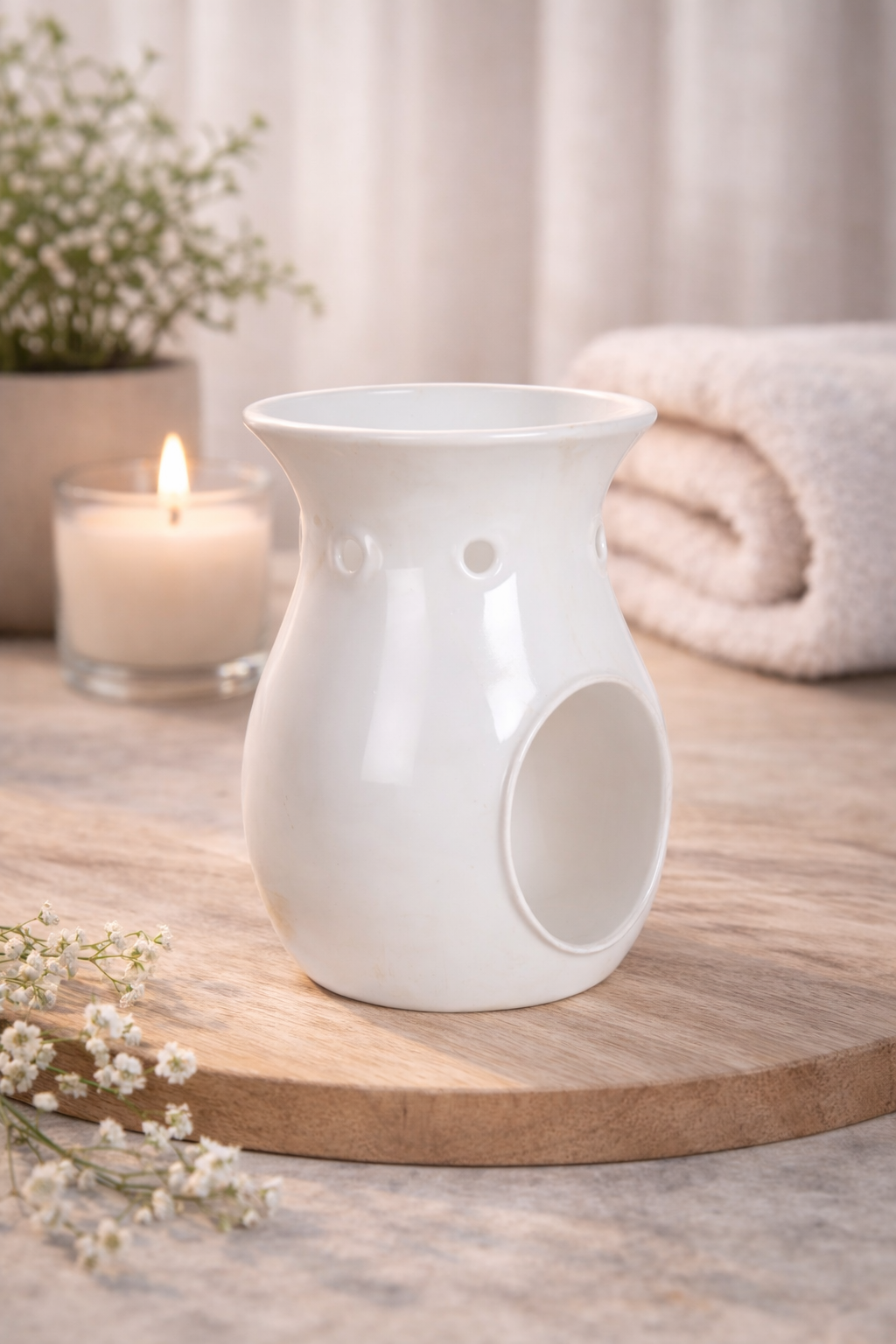 White ceramic wax and oil burner on a wooden surface with a lit candle and flowers in the background