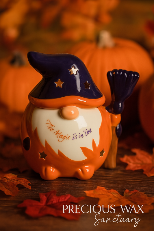 Halloween-themed gnome candle with witch hat and broomstick, surrounded by pumpkins and leaves.