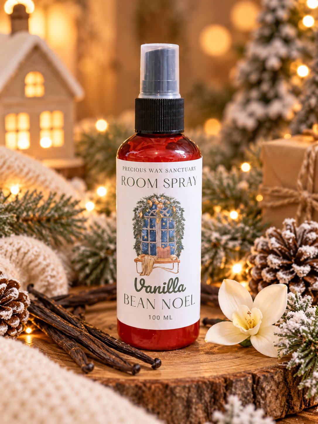 A 100 ml bottle of Vanilla Bean Noel room spray by Precious Wax Sanctuary, styled on a rustic wood slice with vanilla beans, a white flower, pinecones, and a knitted blanket against a warm, festive holiday background with lights and miniature trees.