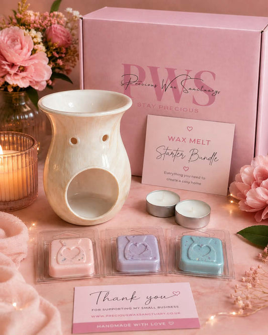 A wax melt starter bundle by PWS arranged on a pink surface with a pink branded box, a cream ceramic warmer, two small tealight candles, three wax melts in clear packaging, and thank you cards, styled with pink flowers and a lit candle.